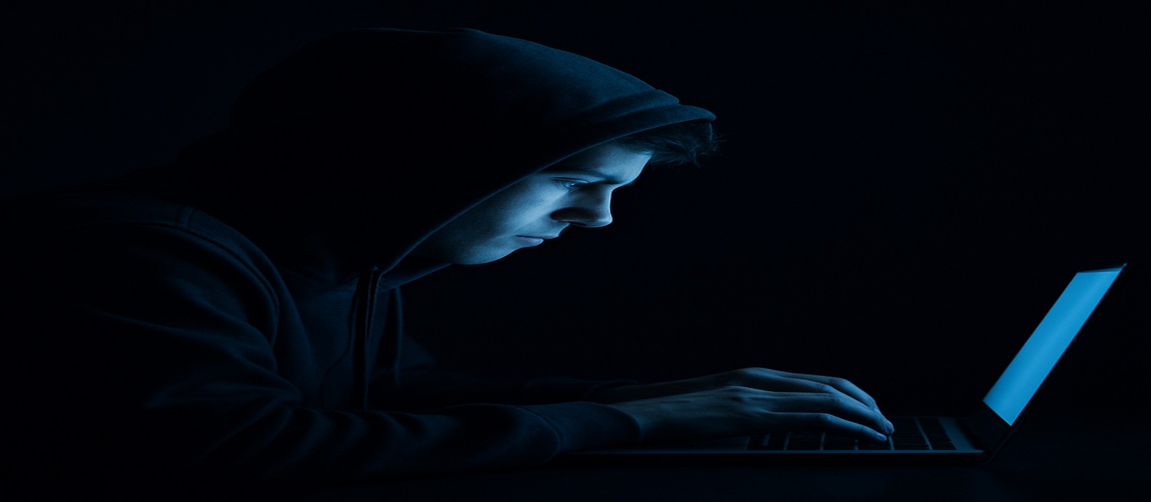 একজন ব্যক্তি অন্ধকার ঘরে ল্যাপটপের সামনে মনোযোগ দিয়ে tk6666 ওয়েবসাইটে অনলাইন গেমিং করছেন